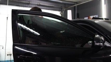 Master installs tint film for car glass with hairdryer and spatula with glare of light. Concept tinting
