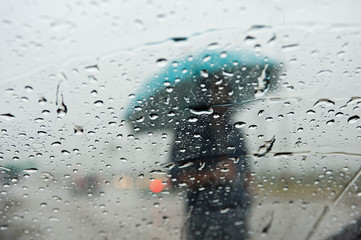 Selective focus at water drops on car glass and blurry people standing in the rain with...