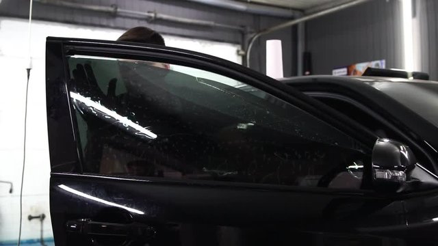 Master installs tint film for car glass with hairdryer and spatula with glare of light. Concept tinting