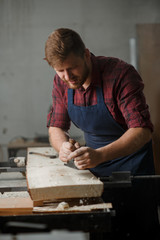 Master carpenter in shirt and apron strokes  plane in workshop