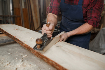 Master carpenter in shirt and apron strokes  plane in workshop. Close up