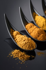 Small black bowls of Indian spices on black background .