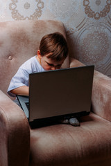 the boy is sitting on a chair and is holding a laptop