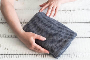 Woman's folding a grey towel to place it on the shelf. Spa and wellness, cotton terry textile.