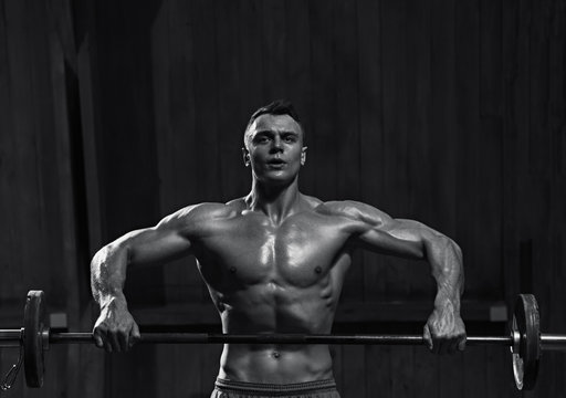 Portrait of strong muscular man working out with barbell, black and white image