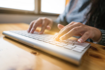 Close-up image of female hands typing text on a wireless keyboard. Business woman working at the office. On wooden table. Copy space