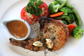 grilled pork chop with vegetable on dish with wood table background