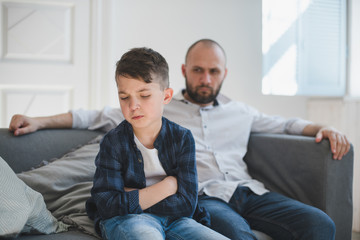 A sad and resentful boy and an angry father in the background.