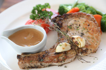 grilled pork chop with vegetable on dish with wood table background