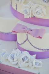 Dettaglio di Bellissima torta nuziale ornata con dei fiori in cima - elementi di decorazioni lilla impreziositi da un diadema e un fiocco di glassa