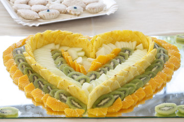 Presentazione di frutta a forma di cuore, con sfondo dolcetti sardi