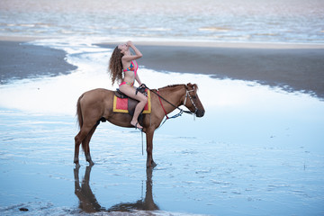 Happy smiling attractive blond curly hair woman riding a horse on the Beach, relaxing time concept.