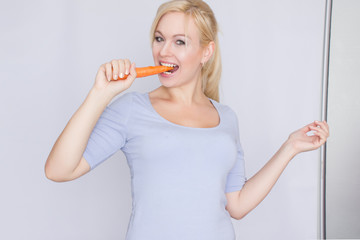Young blond woman biting young large carrots with her teeth