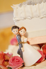 Cake topper di sposi simpatico con i due legati da una catena affianco a torta nuziale di panna e granella © alex.pin