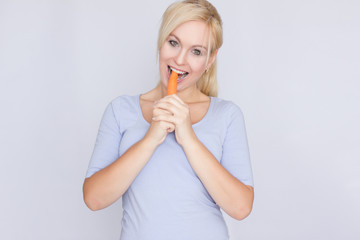 Young blond woman biting young large carrots with her teeth