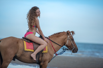 Happy smiling attractive blond curly hair woman riding a horse on the Beach, relaxing time concept.