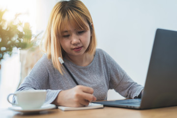Beautiful young smiling asian woman working on laptop while sitting in a living room at home. Asian business woman working in her home office. Enjoying time at home.