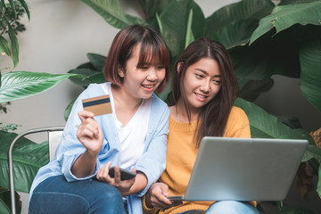 Close up of a couple young Asian women using her credit card while they do shopping online with her laptop. Young women shopping online in the garden holding her credit card. Shopping online concept.