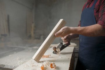 Master carpenter in  shirt and apron works as an ax in workshop. Close up