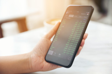 Female hand with smartphone trading stock online in coffee shop , Business concept