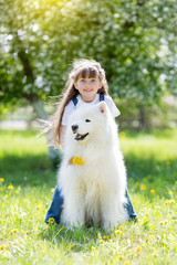Little girl with a big white dog in the park. A beautiful 5 year old girl in jeans hugs her favorite dog during a summer walk.