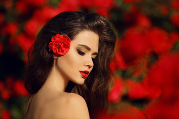 Outdoors portrait of Natural Beauty woman in red roses. Sensual female with rose flowers in hair. Sexy brunette with makeup over sunset blossom park. Passion and expression. Spanish flamenco style. - obrazy, fototapety, plakaty
