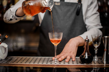 Bartender pourring an alcoholic drink into the cocktail glass
