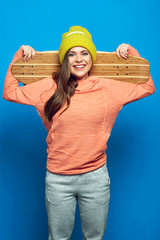 Portrait of modern girl holding skateboard wearing winter cap.