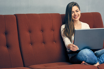 Smiling young woman working with laptop on sofa.