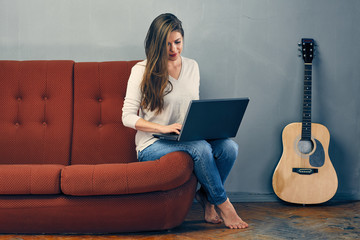 Working woman using laptop on sofa with grey wall on background.
