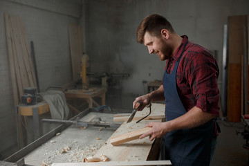Master carpenter in  shirt and apron works as an ax in workshop