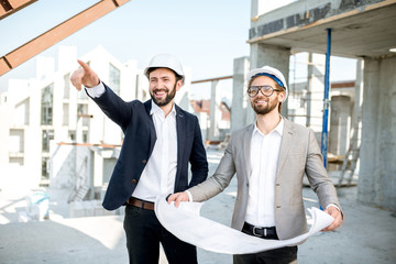 Two business men or engeneers working with house drawings on the structure during the construction process outdoors