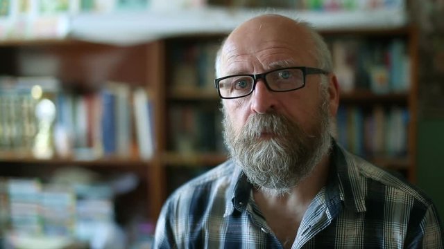 elderly bald man dresses glasses and looks at the camera