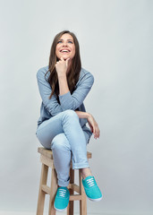 Smiling young woman sitting on stool with crossed legs.