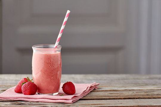 Yogurt and strawberry smoothie in jar with drinking straw on wooden table