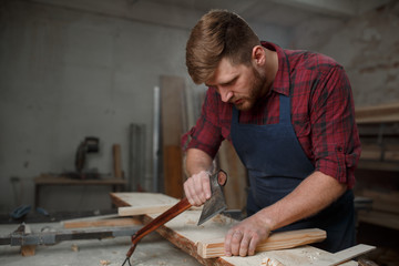 Master carpenter in  shirt and apron works as an ax in workshop