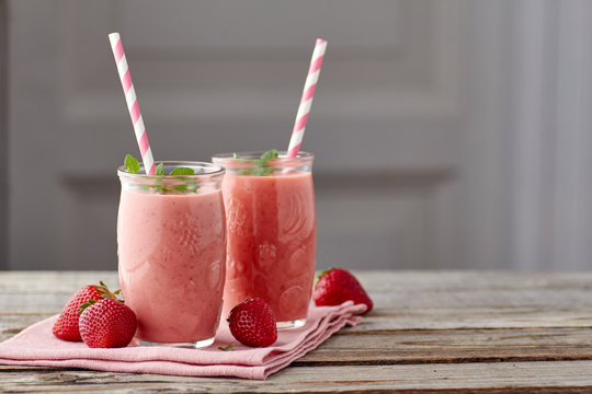 Yogurt and strawberry smoothie in two jars with drinking straw on wooden table