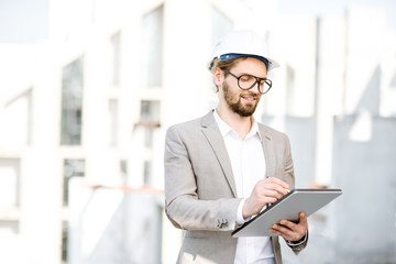 Handsome engineer working with tablet standing on the structure site with a new house on the background