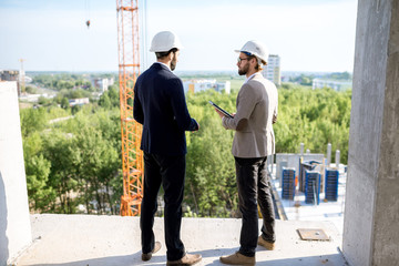Two engineers or architects supervising the process of residential building construction standing...
