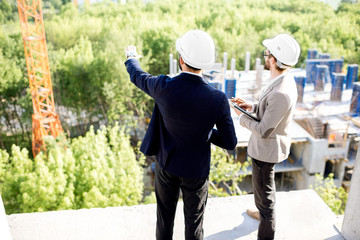 Two engineers or architects supervising the process of residential building construction standing...