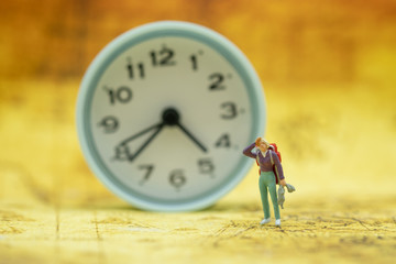 Travel and Time Concept. Traveler miniature figure with backpack and jacket standing on world map with vintage round clock as background.