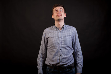 A dark haired white man looking up and smile in a plaid shirt and jeans on a black isolated background