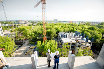 Top view on the construction site of residential buildings on the green area with two workers looking on the construction process