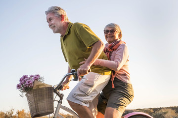 elderly senior caucasian couple play and enjoy leisure activity outdoor in lifestyle vacation. man and woman retired go on a vintage bike like children age. tropical palm background.