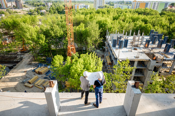 Top view on the construction site of residential buildings on the green area with two workers looking on the construction process