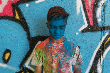 Teen smiling with hands in front of his face, is painted blue with a graffiti