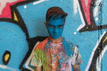 Teen smiling with hands in front of his face, is painted blue with a graffiti