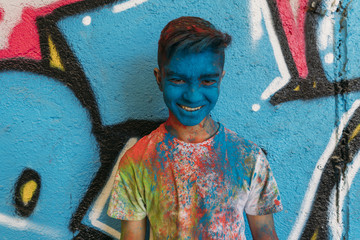 Teen smiling with hands in front of his face, is painted blue with a graffiti