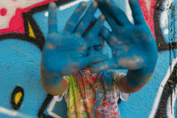 Teen smiling with hands in front of his face, is painted blue with a graffiti