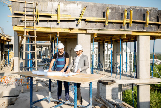 Engineer with worker in uniform working with architectural drawings at the table on the construction site outdoors